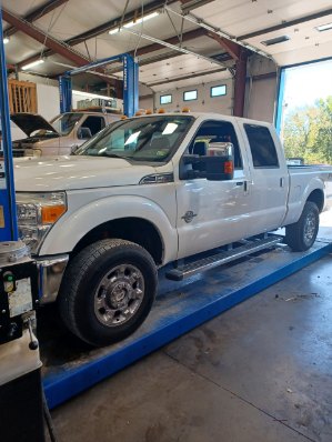 A white Ford Super Duty pickup parked over a lift inside the shop